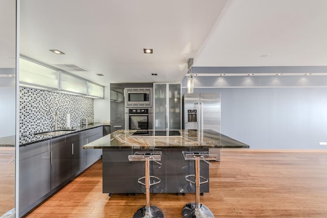 kitchen featuring sink, a breakfast bar area, dark stone counters, light wood-type flooring, and stainless steel appliances