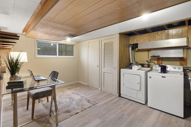 clothes washing area featuring light hardwood / wood-style flooring, washer and clothes dryer, and wood walls