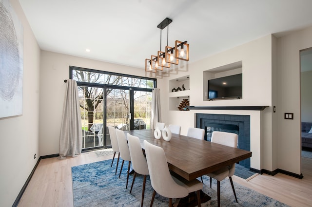 dining room featuring a tile fireplace, built in features, a chandelier, and light wood-type flooring