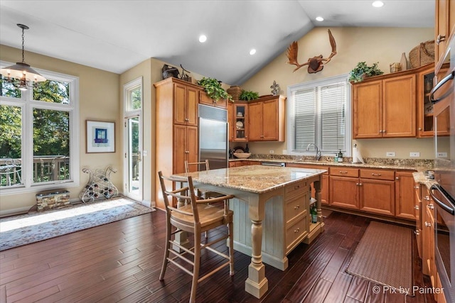 kitchen featuring light stone countertops, hanging light fixtures, dark hardwood / wood-style flooring, stainless steel built in refrigerator, and a kitchen island