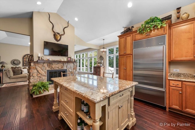 kitchen featuring vaulted ceiling, pendant lighting, a center island, built in refrigerator, and a stone fireplace