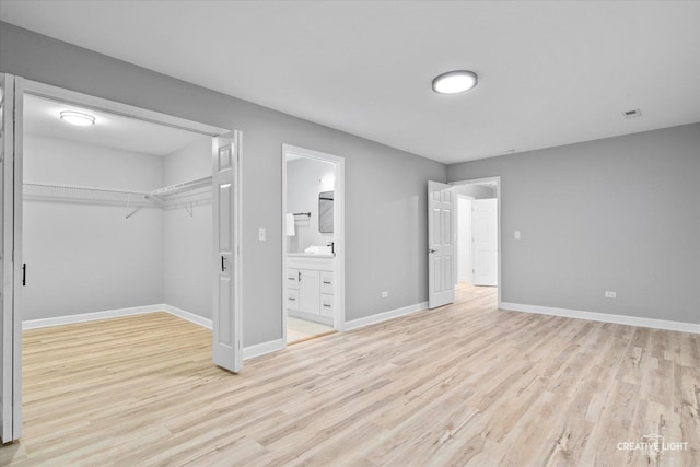 unfurnished bedroom featuring ensuite bathroom, a closet, and light hardwood / wood-style floors