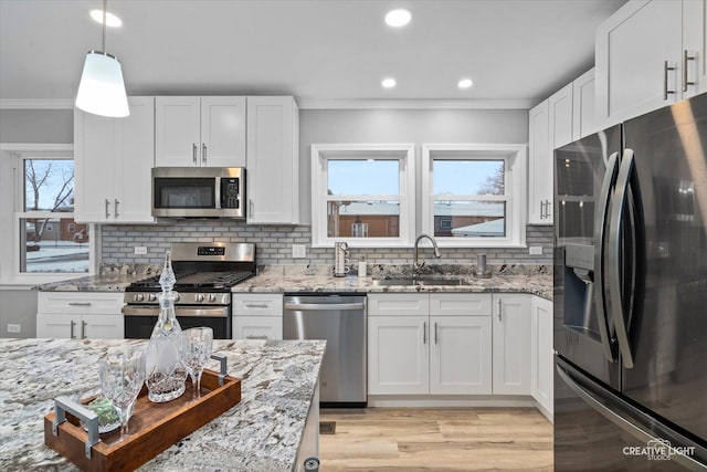 kitchen featuring light stone countertops, sink, stainless steel appliances, pendant lighting, and white cabinets