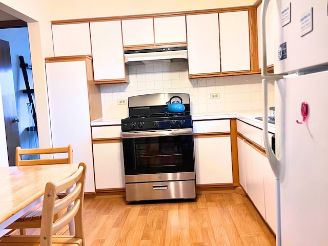 kitchen with white refrigerator, stainless steel gas stove, tasteful backsplash, light hardwood / wood-style floors, and white cabinetry