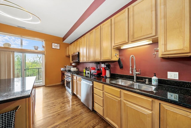 kitchen with appliances with stainless steel finishes, light wood-type flooring, sink, decorative light fixtures, and dark stone countertops