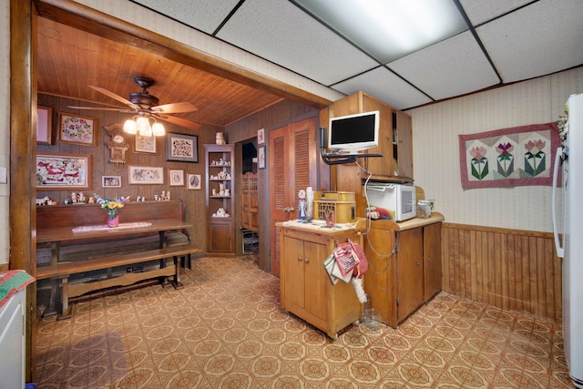 kitchen with ceiling fan, white fridge, a drop ceiling, and wooden walls