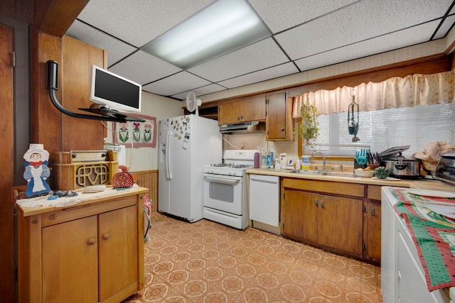 kitchen with wood walls, white appliances, a paneled ceiling, and sink