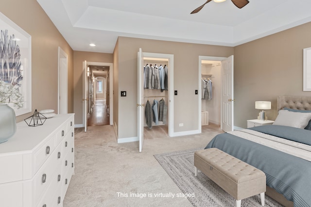 carpeted bedroom featuring a tray ceiling, a walk in closet, ceiling fan, and a closet