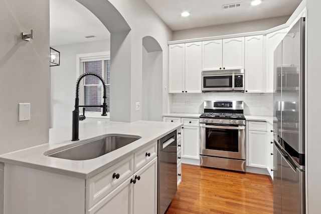 kitchen with sink, stainless steel appliances, light hardwood / wood-style flooring, decorative backsplash, and white cabinets