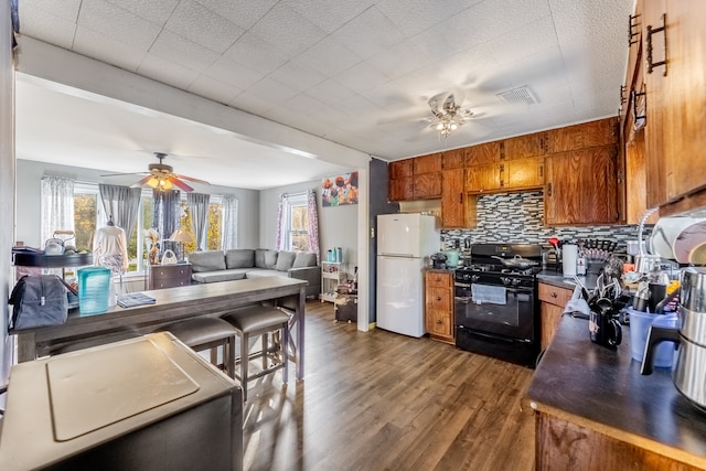 kitchen featuring white refrigerator, dark hardwood / wood-style floors, ceiling fan, tasteful backsplash, and black range with gas cooktop