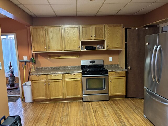 kitchen featuring dark countertops, a drop ceiling, stainless steel appliances, and light wood finished floors