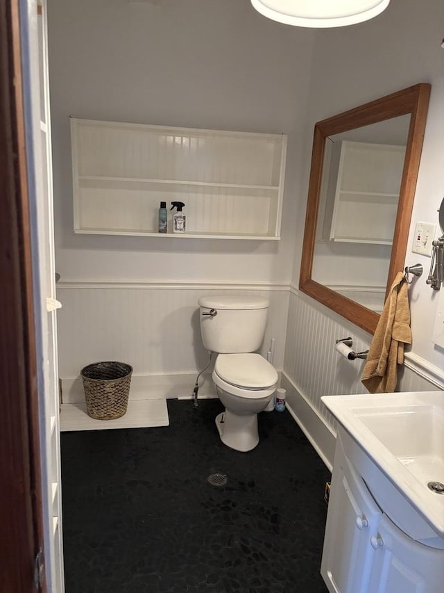 bathroom with vanity, wainscoting, a decorative wall, and toilet