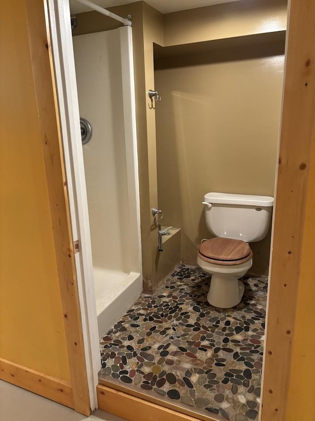 bathroom featuring stone finish floor, toilet, and a shower stall