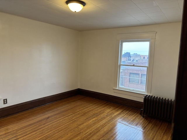 spare room with wood finished floors, baseboards, and radiator heating unit