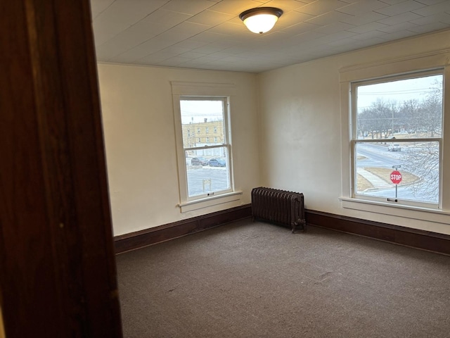 carpeted spare room featuring baseboards, a wealth of natural light, and radiator