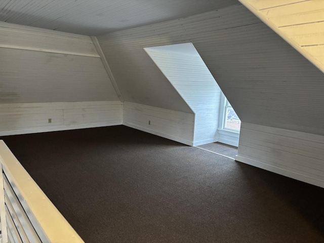 additional living space with dark colored carpet, vaulted ceiling, and wood walls