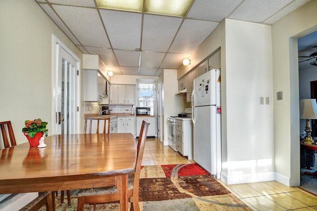 dining space featuring a paneled ceiling, ceiling fan, sink, and light tile patterned flooring