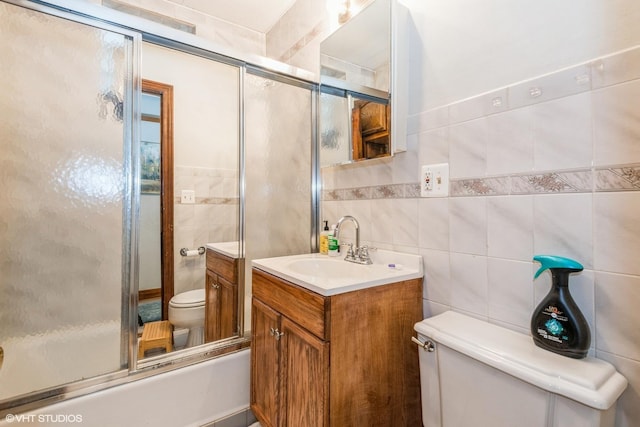 full bathroom featuring vanity, toilet, bath / shower combo with glass door, and tile walls