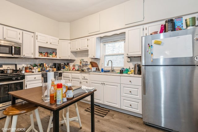 kitchen featuring appliances with stainless steel finishes, light wood-type flooring, backsplash, sink, and white cabinetry