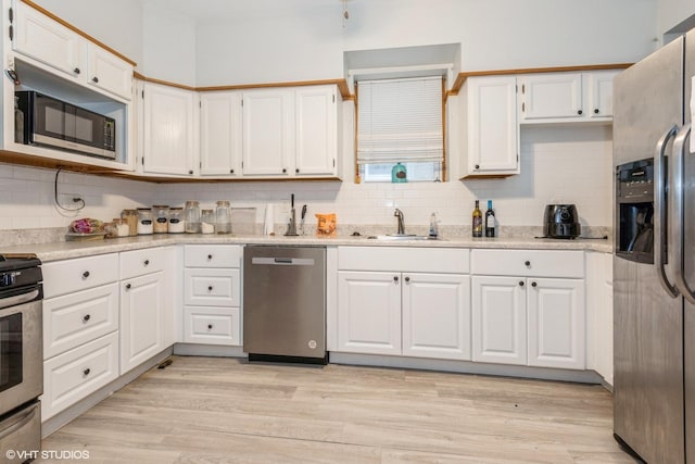 kitchen featuring white cabinets, sink, decorative backsplash, light wood-type flooring, and appliances with stainless steel finishes