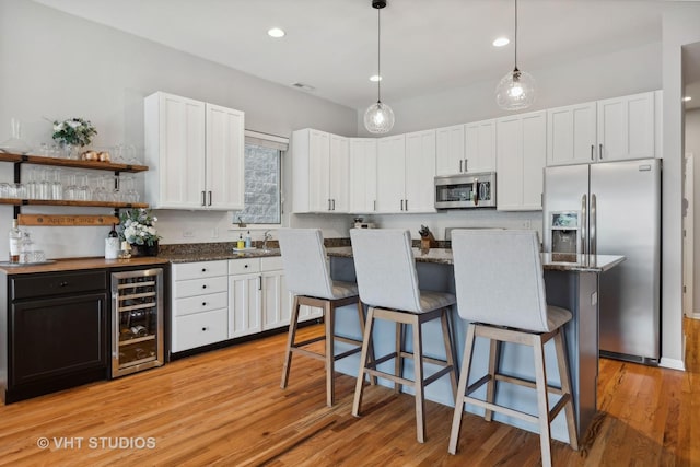 kitchen with white cabinets, stainless steel appliances, wine cooler, and light hardwood / wood-style flooring