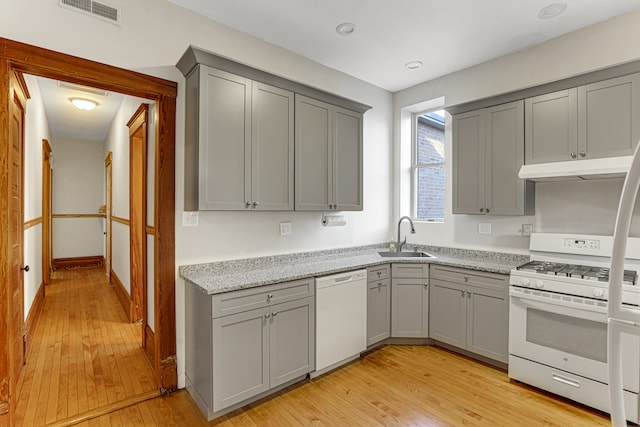 kitchen featuring gray cabinetry, sink, light stone counters, light hardwood / wood-style flooring, and white appliances