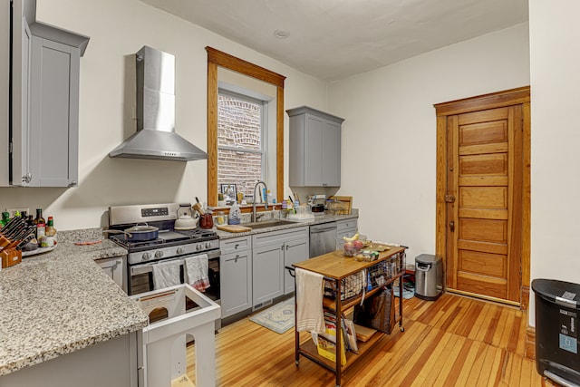 kitchen featuring sink, wall chimney exhaust hood, gray cabinets, appliances with stainless steel finishes, and light wood-type flooring