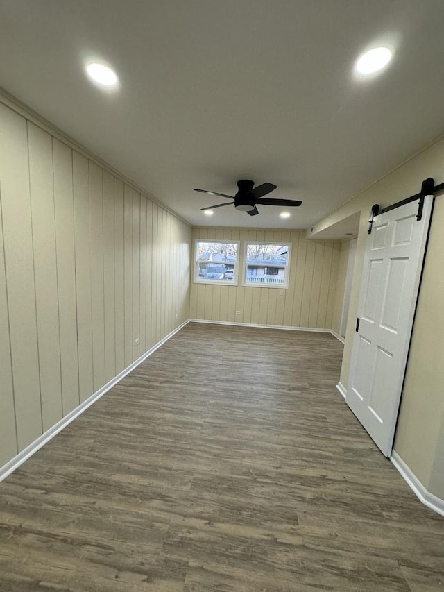 empty room with a barn door, wood walls, ceiling fan, and dark hardwood / wood-style floors