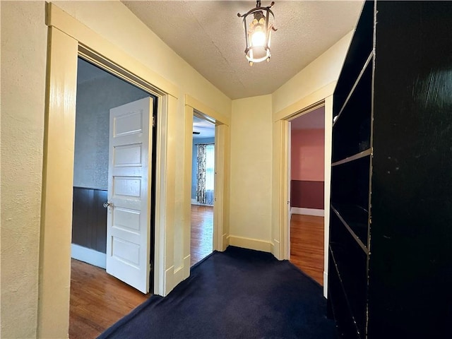 hallway featuring dark colored carpet and a textured ceiling