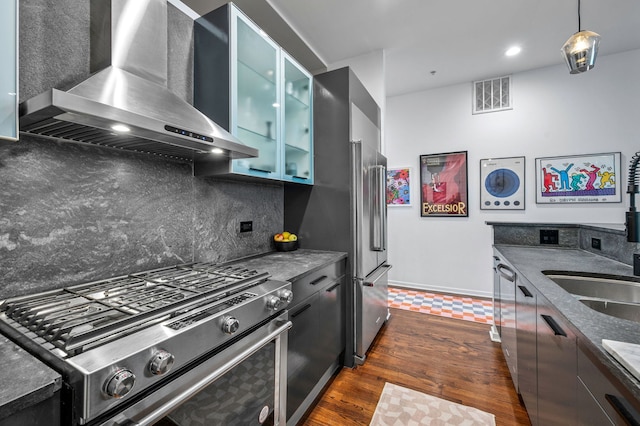 kitchen featuring wall chimney exhaust hood, tasteful backsplash, appliances with stainless steel finishes, pendant lighting, and dark stone counters