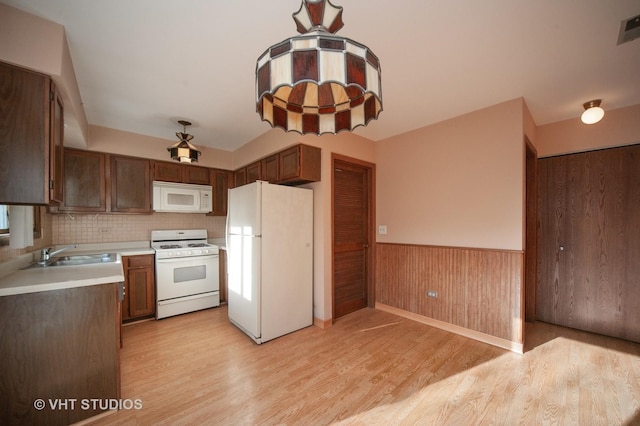 kitchen with light wood-type flooring, white appliances, wooden walls, and sink