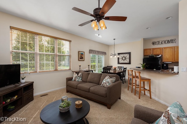 living area with ceiling fan with notable chandelier, baseboards, and light colored carpet