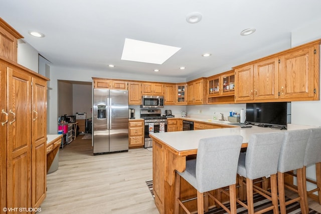 kitchen with a skylight, stainless steel appliances, kitchen peninsula, light hardwood / wood-style floors, and a breakfast bar