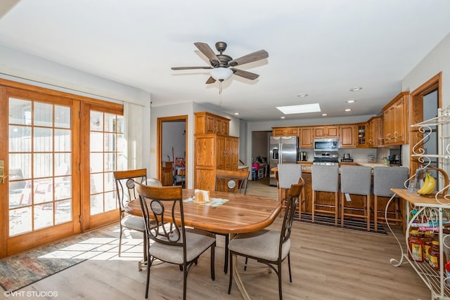 dining room featuring a skylight, light hardwood / wood-style flooring, and ceiling fan