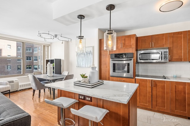 kitchen featuring hanging light fixtures, a kitchen island, appliances with stainless steel finishes, tasteful backsplash, and light hardwood / wood-style floors