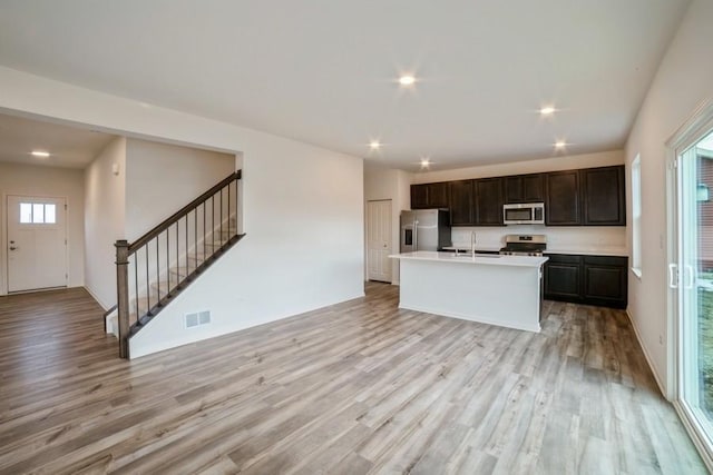 kitchen with sink, light hardwood / wood-style flooring, a kitchen island with sink, dark brown cabinets, and appliances with stainless steel finishes