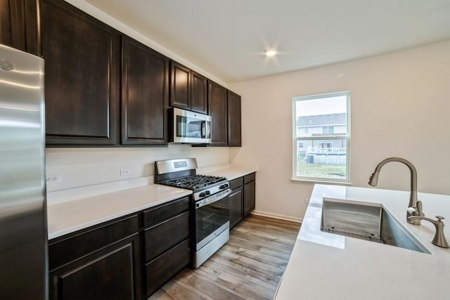 kitchen with dark brown cabinets, light wood-type flooring, sink, and appliances with stainless steel finishes