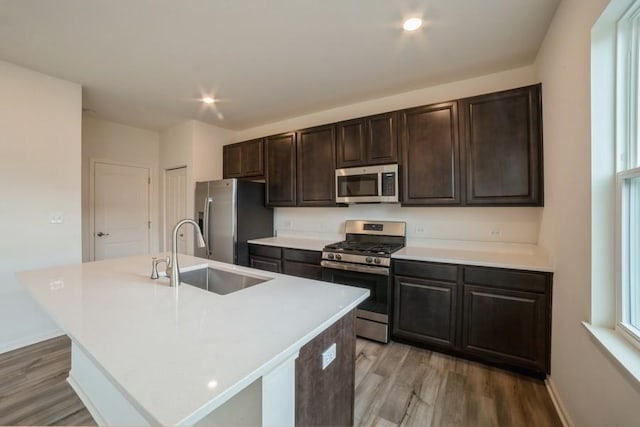 kitchen featuring dark brown cabinets, stainless steel appliances, sink, a center island with sink, and light hardwood / wood-style flooring