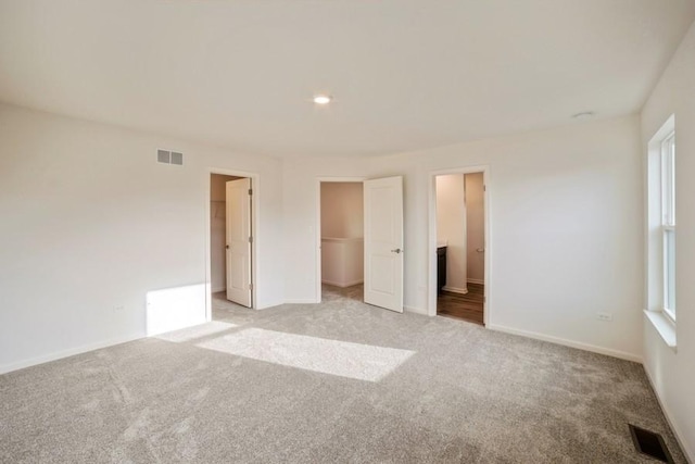 unfurnished bedroom with a walk in closet, light carpet, a closet, and ensuite bath