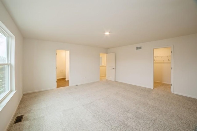 unfurnished bedroom featuring connected bathroom, a walk in closet, light carpet, and a closet