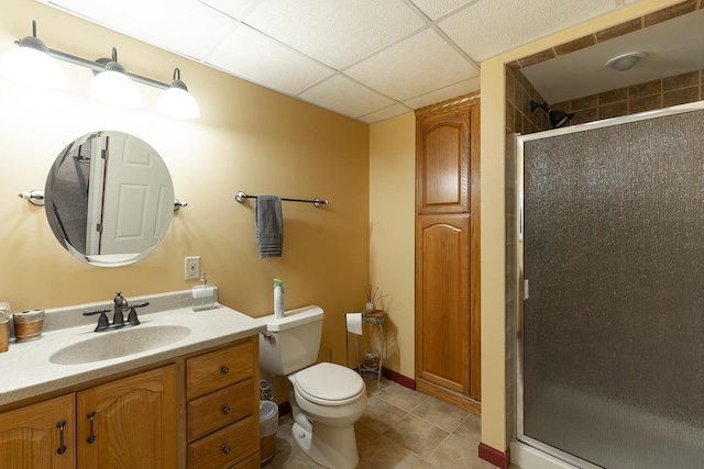 bathroom featuring a drop ceiling, tile patterned flooring, toilet, a shower with door, and vanity