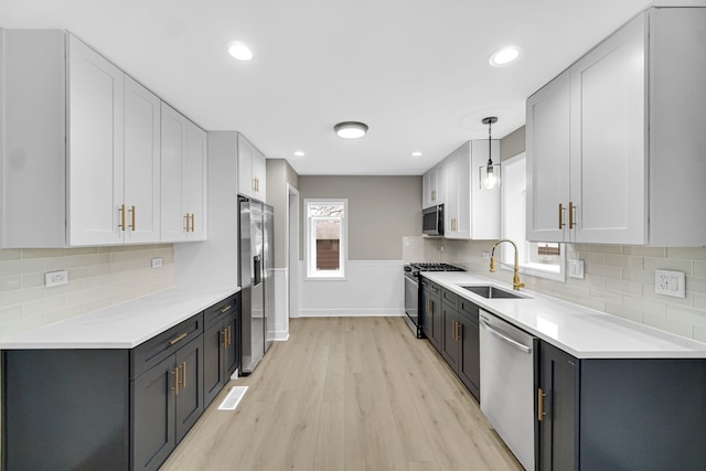 kitchen with sink, hanging light fixtures, stainless steel appliances, white cabinets, and light wood-type flooring