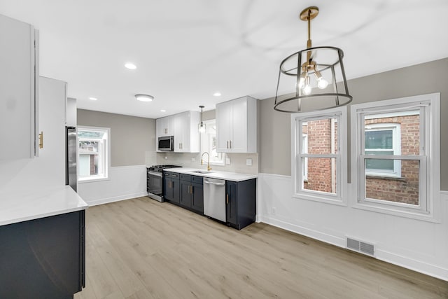 kitchen featuring appliances with stainless steel finishes, sink, pendant lighting, light hardwood / wood-style floors, and white cabinetry