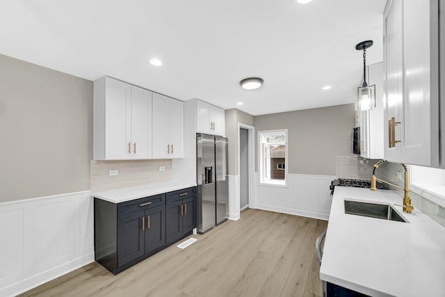 kitchen with hanging light fixtures, tasteful backsplash, stainless steel refrigerator with ice dispenser, white cabinets, and light wood-type flooring