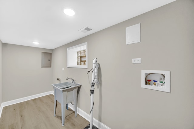 clothes washing area with electric panel, hookup for a washing machine, light hardwood / wood-style floors, and sink