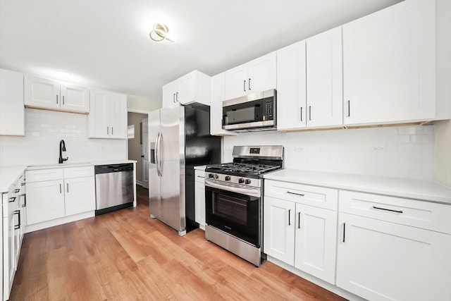 kitchen with backsplash, stainless steel appliances, sink, white cabinets, and light hardwood / wood-style floors