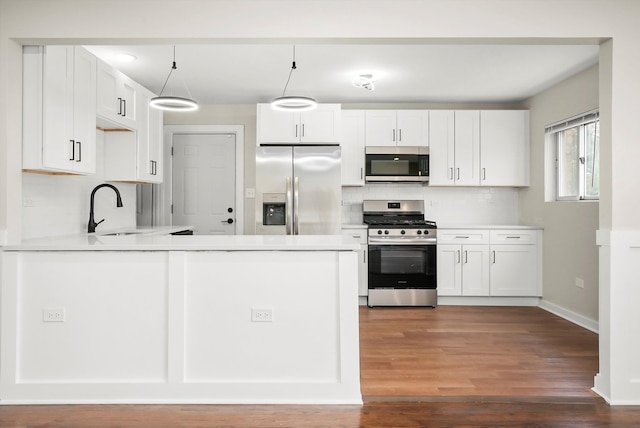 kitchen featuring white cabinets, hanging light fixtures, sink, appliances with stainless steel finishes, and kitchen peninsula