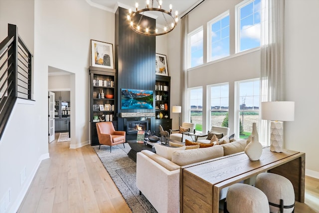 living room with a towering ceiling, a healthy amount of sunlight, a notable chandelier, and light wood-type flooring