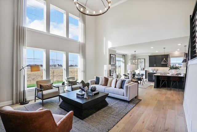 living room featuring a towering ceiling, light hardwood / wood-style floors, an inviting chandelier, and a healthy amount of sunlight