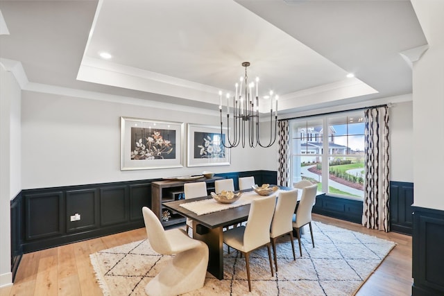 dining area with an inviting chandelier, a tray ceiling, light hardwood / wood-style flooring, and crown molding